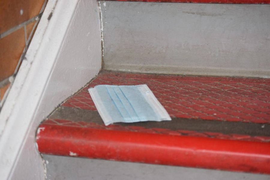 A disposable mask lays on a second floor stairway after being discarded.