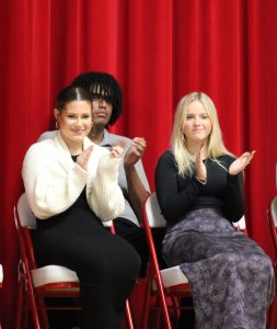 NHS treasurer Manny Tewodros (back), and members Lauren Flanagan and Anna Floyd (front) on stage during the NHS induction ceremony Nov. 19. Flanagan read a description of the pillar of service, and Floyd read leadership.