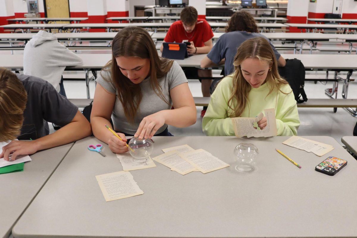 Juniors Kendall Kimes and Rylee Lamp trace and cut book pages into circles to make paper flowers May 1 in the cafeteria.